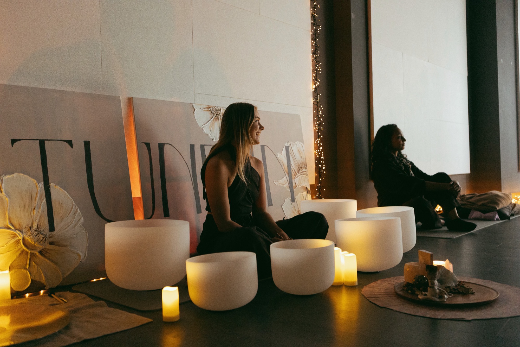 Two people sitting side by side among candlelit crystal singing bowls at a Tune In session